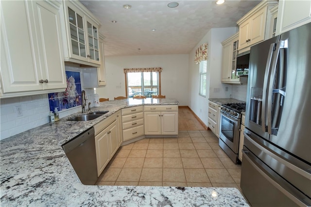 kitchen with kitchen peninsula, appliances with stainless steel finishes, light stone countertops, sink, and light tile patterned floors