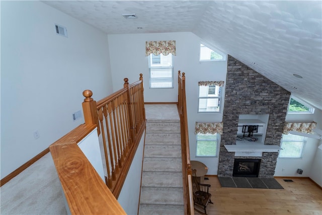 stairway featuring a stone fireplace, carpet floors, and vaulted ceiling