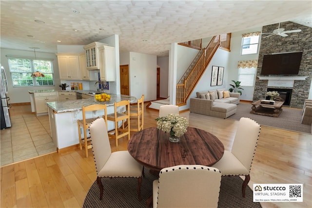 dining room featuring a fireplace, light hardwood / wood-style flooring, ceiling fan, and sink