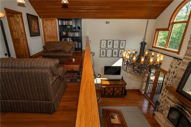 living room featuring wood-type flooring, a stone fireplace, wooden ceiling, and a notable chandelier