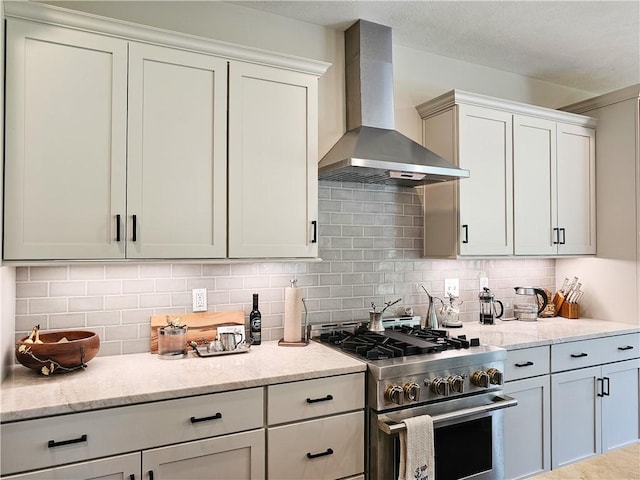 kitchen with decorative backsplash, white cabinetry, high end stainless steel range oven, and wall chimney exhaust hood