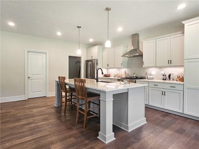 kitchen featuring a center island with sink, white cabinetry, high quality fridge, and wall chimney exhaust hood