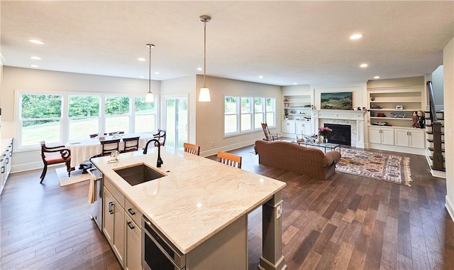 kitchen featuring light stone counters, sink, pendant lighting, a center island with sink, and built in features