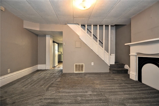 unfurnished living room featuring dark colored carpet and a paneled ceiling