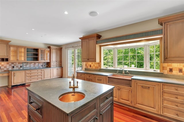 kitchen with dark hardwood / wood-style flooring, decorative backsplash, a center island with sink, and sink