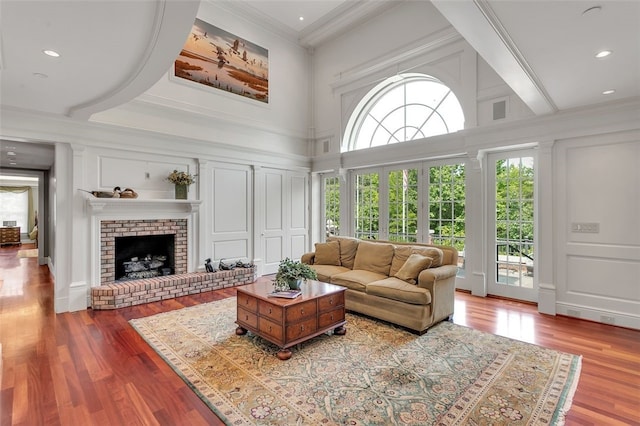 living room with a towering ceiling, crown molding, hardwood / wood-style flooring, beamed ceiling, and a fireplace