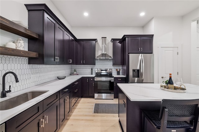 kitchen featuring light hardwood / wood-style flooring, backsplash, wall chimney exhaust hood, appliances with stainless steel finishes, and sink