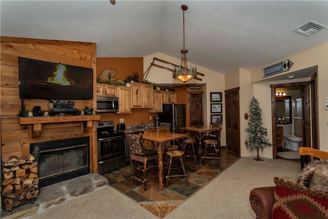 kitchen featuring light brown cabinets, dark carpet, lofted ceiling, a tiled fireplace, and black appliances