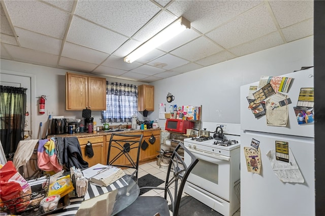 kitchen with a drop ceiling, sink, white appliances, and light tile patterned floors