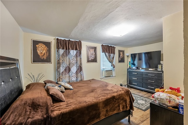 bedroom with cooling unit, a textured ceiling, and light wood-type flooring