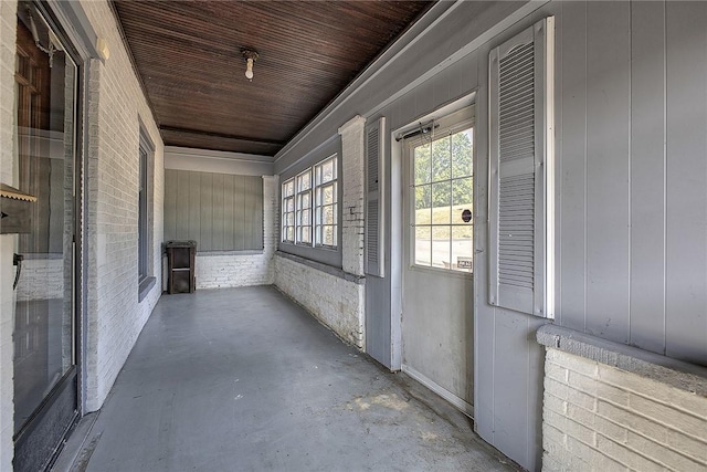 hallway featuring brick wall, concrete flooring, and wooden ceiling