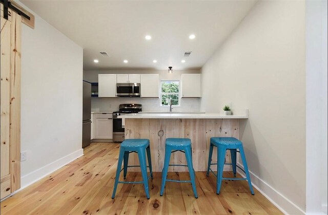 kitchen with a barn door, appliances with stainless steel finishes, light hardwood / wood-style floors, a kitchen bar, and white cabinetry