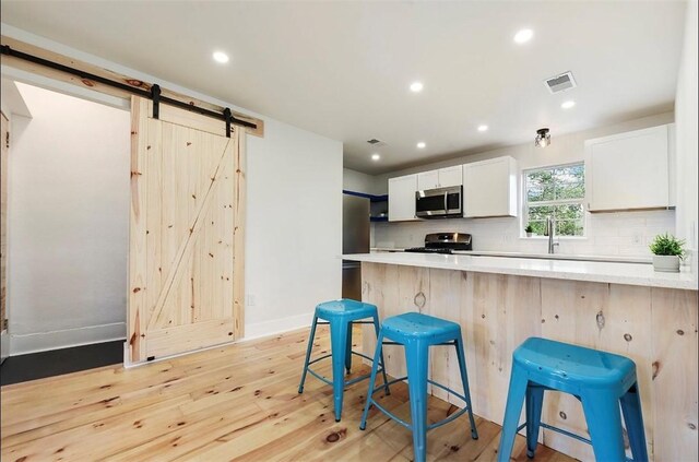 kitchen featuring a breakfast bar area, a barn door, light wood-type flooring, white cabinetry, and stainless steel appliances