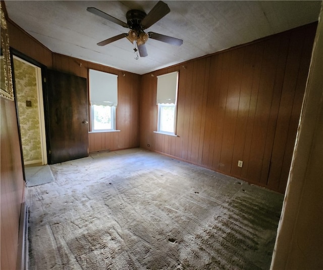 unfurnished room with wooden walls, light colored carpet, and ceiling fan