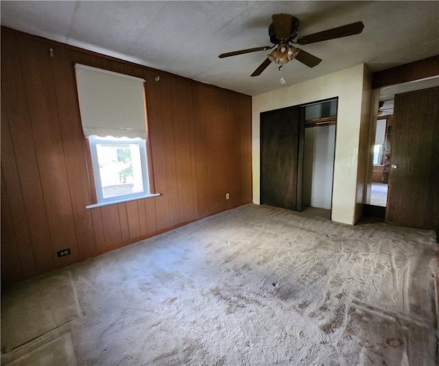 unfurnished bedroom featuring ceiling fan, light colored carpet, and wood walls