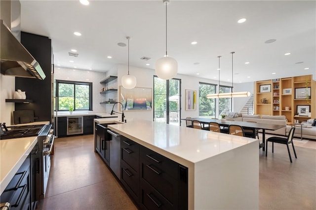 kitchen with wall chimney exhaust hood, hanging light fixtures, backsplash, a large island with sink, and double oven range