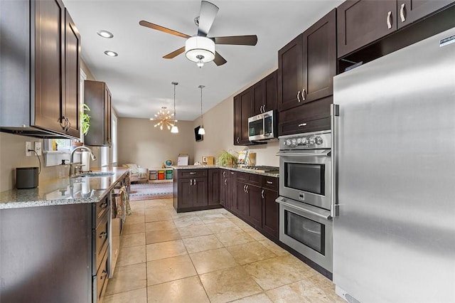 kitchen featuring light stone countertops, appliances with stainless steel finishes, dark brown cabinets, sink, and decorative light fixtures