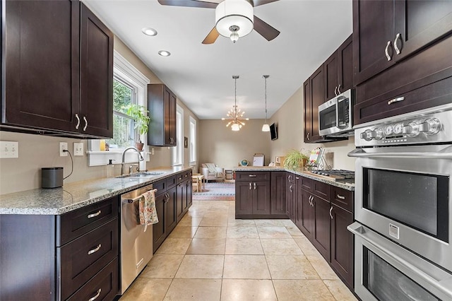 kitchen with light stone countertops, appliances with stainless steel finishes, sink, pendant lighting, and light tile patterned flooring