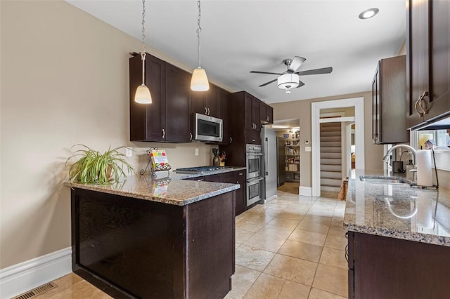 kitchen featuring dark brown cabinetry, sink, hanging light fixtures, light stone counters, and appliances with stainless steel finishes