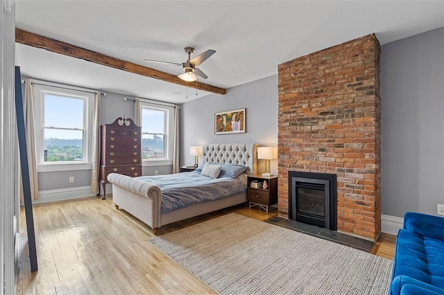 bedroom with ceiling fan, beam ceiling, light wood-type flooring, and a fireplace