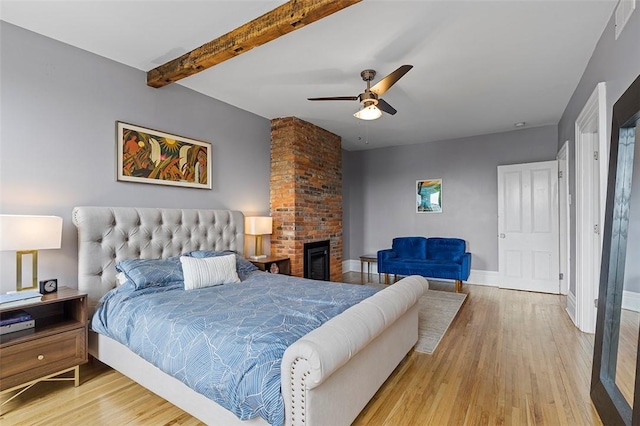 bedroom featuring wood-type flooring, a brick fireplace, ceiling fan, and beam ceiling