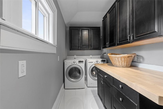 clothes washing area with washer and dryer, light tile patterned floors, and cabinets