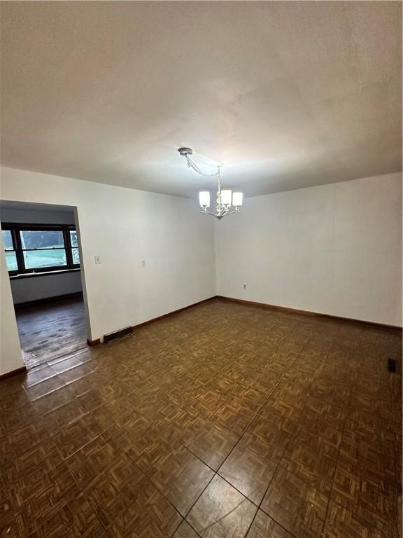 unfurnished room featuring a notable chandelier, dark parquet floors, and a textured ceiling