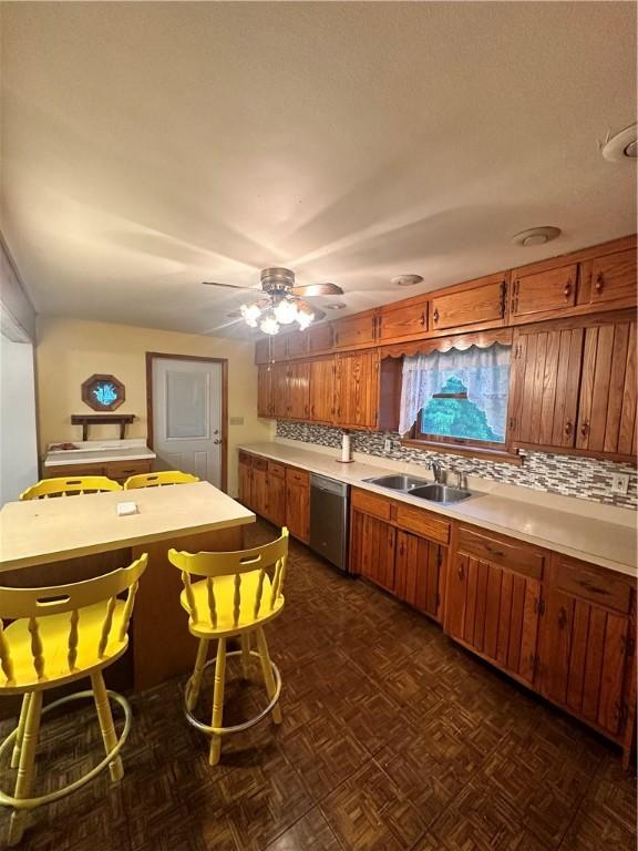 kitchen featuring dark parquet flooring, backsplash, ceiling fan, stainless steel dishwasher, and sink