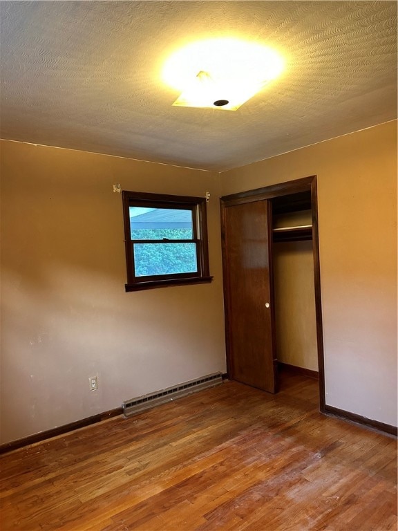 unfurnished bedroom featuring wood-type flooring, baseboard heating, a closet, and a textured ceiling