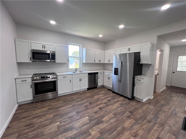 kitchen with appliances with stainless steel finishes, white cabinetry, dark hardwood / wood-style floors, and sink