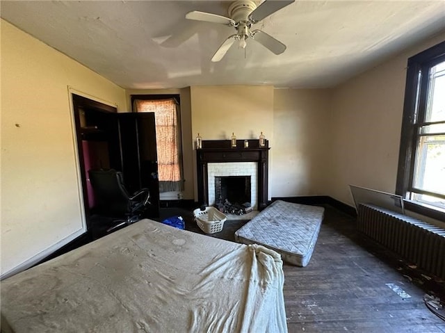 unfurnished bedroom with hardwood / wood-style flooring, radiator heating unit, a brick fireplace, and ceiling fan