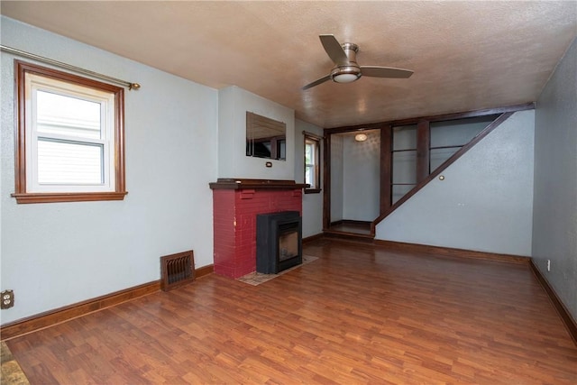 unfurnished living room featuring hardwood / wood-style flooring, ceiling fan, a brick fireplace, and a textured ceiling