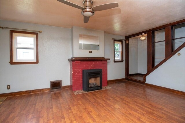 unfurnished living room featuring ceiling fan, a brick fireplace, and hardwood / wood-style floors