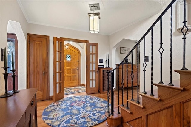 foyer with ornamental molding, french doors, and light wood-type flooring