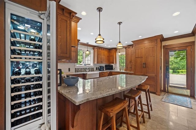 kitchen featuring pendant lighting, tasteful backsplash, ornamental molding, light stone countertops, and a kitchen bar