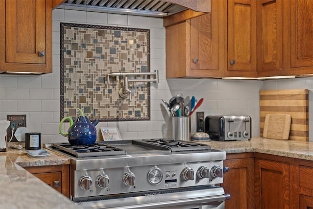 kitchen featuring light stone counters, backsplash, stainless steel stove, and ventilation hood