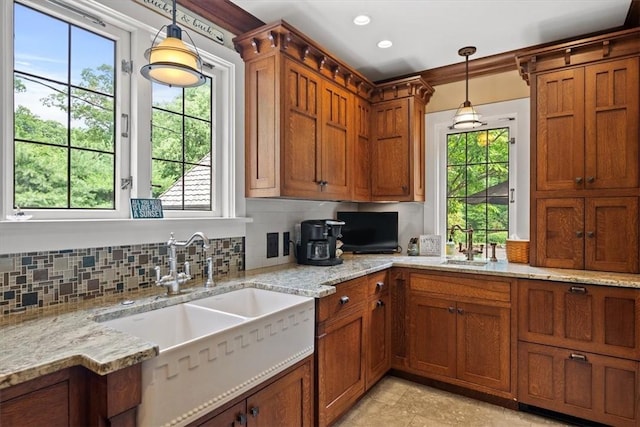 kitchen featuring pendant lighting, backsplash, light stone countertops, and sink