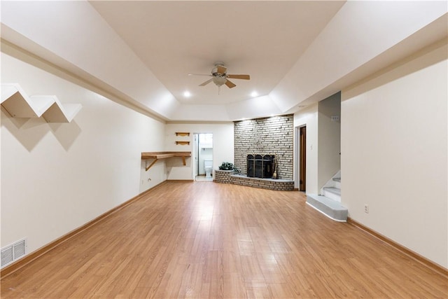 unfurnished living room featuring a brick fireplace, ceiling fan, a raised ceiling, and light hardwood / wood-style flooring