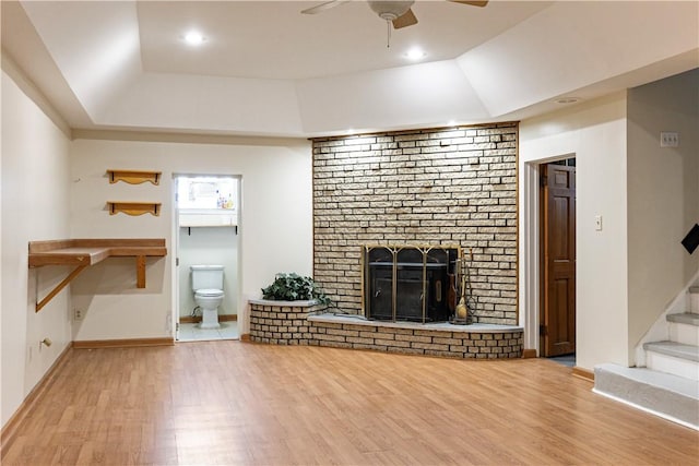 unfurnished living room featuring hardwood / wood-style floors, ceiling fan, a brick fireplace, and a tray ceiling