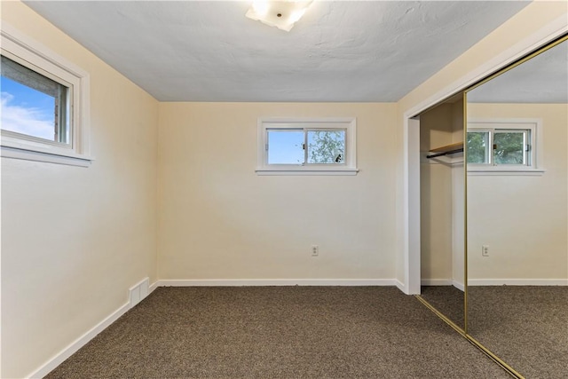 unfurnished bedroom featuring dark colored carpet, a closet, and multiple windows