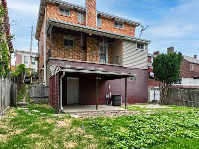 rear view of property with a balcony, a yard, a patio, and central AC