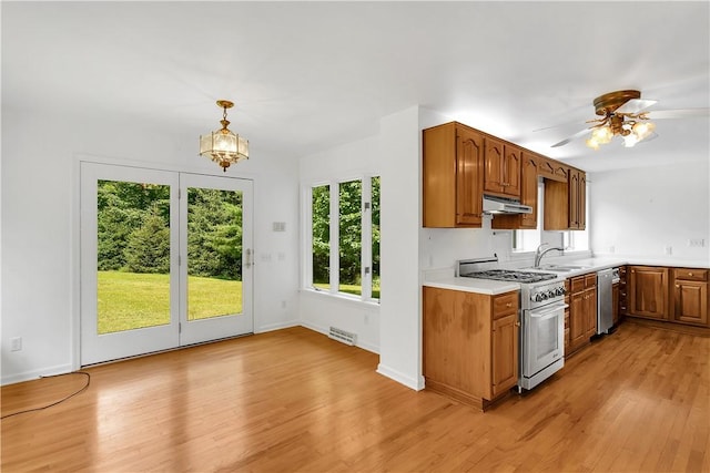 kitchen with ceiling fan with notable chandelier, stainless steel appliances, sink, decorative light fixtures, and light hardwood / wood-style flooring