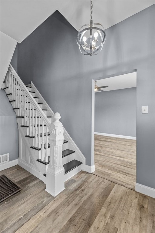 staircase featuring ceiling fan with notable chandelier and wood-type flooring