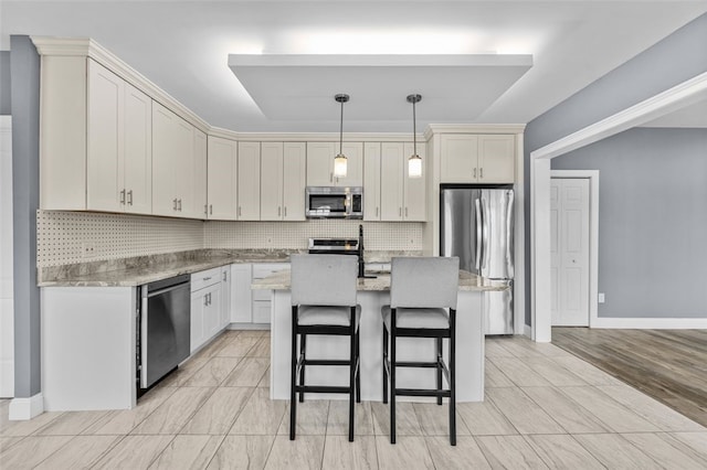 kitchen with stainless steel appliances, backsplash, hanging light fixtures, light stone countertops, and a kitchen island with sink