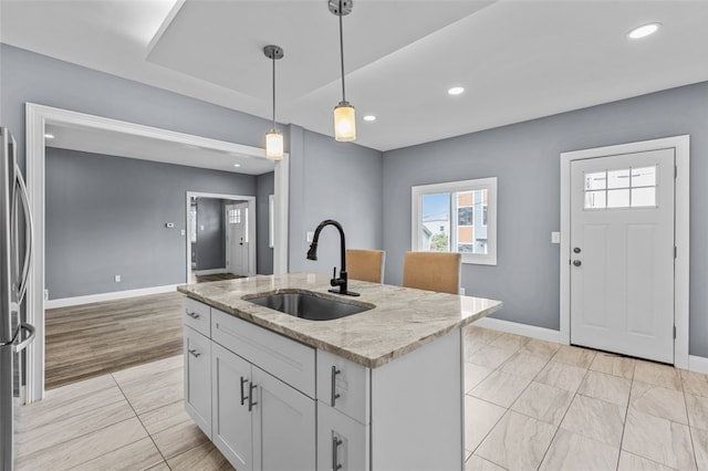 kitchen featuring light stone countertops, decorative light fixtures, a center island with sink, white cabinets, and sink