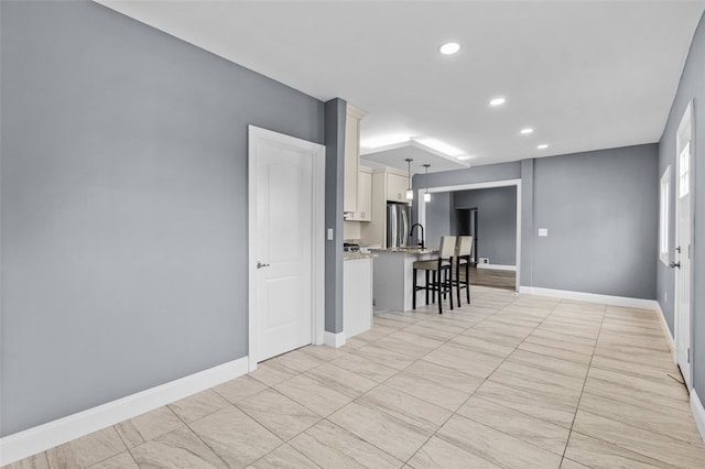 kitchen featuring a breakfast bar, stainless steel fridge, white cabinetry, and decorative light fixtures