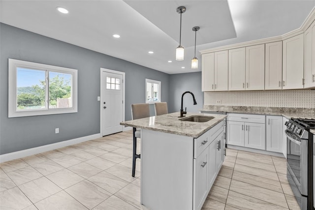 kitchen with light stone countertops, stainless steel gas range oven, a center island with sink, tasteful backsplash, and sink