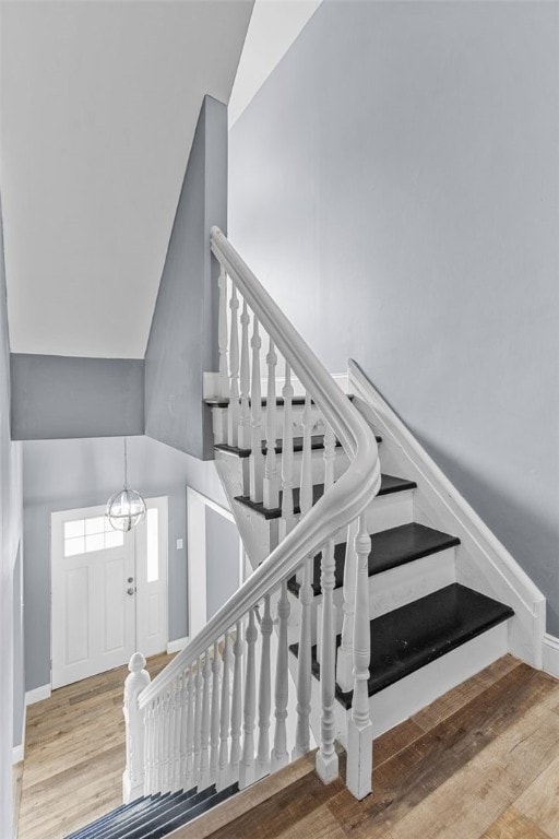 stairway featuring an inviting chandelier, lofted ceiling, and wood-type flooring