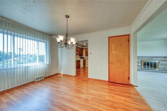 unfurnished dining area featuring ornamental molding, light wood-type flooring, a fireplace, and a chandelier