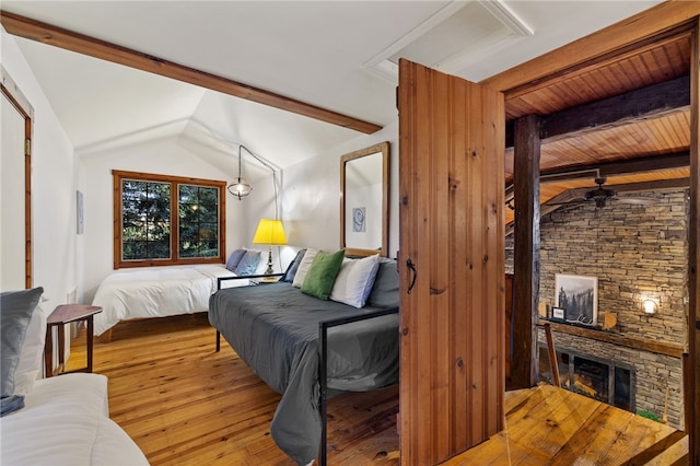 bedroom with a stone fireplace, lofted ceiling with beams, light hardwood / wood-style floors, and wooden ceiling